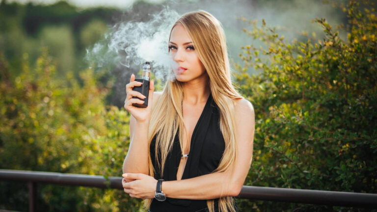 Young woman vaping outdoors among greenery.