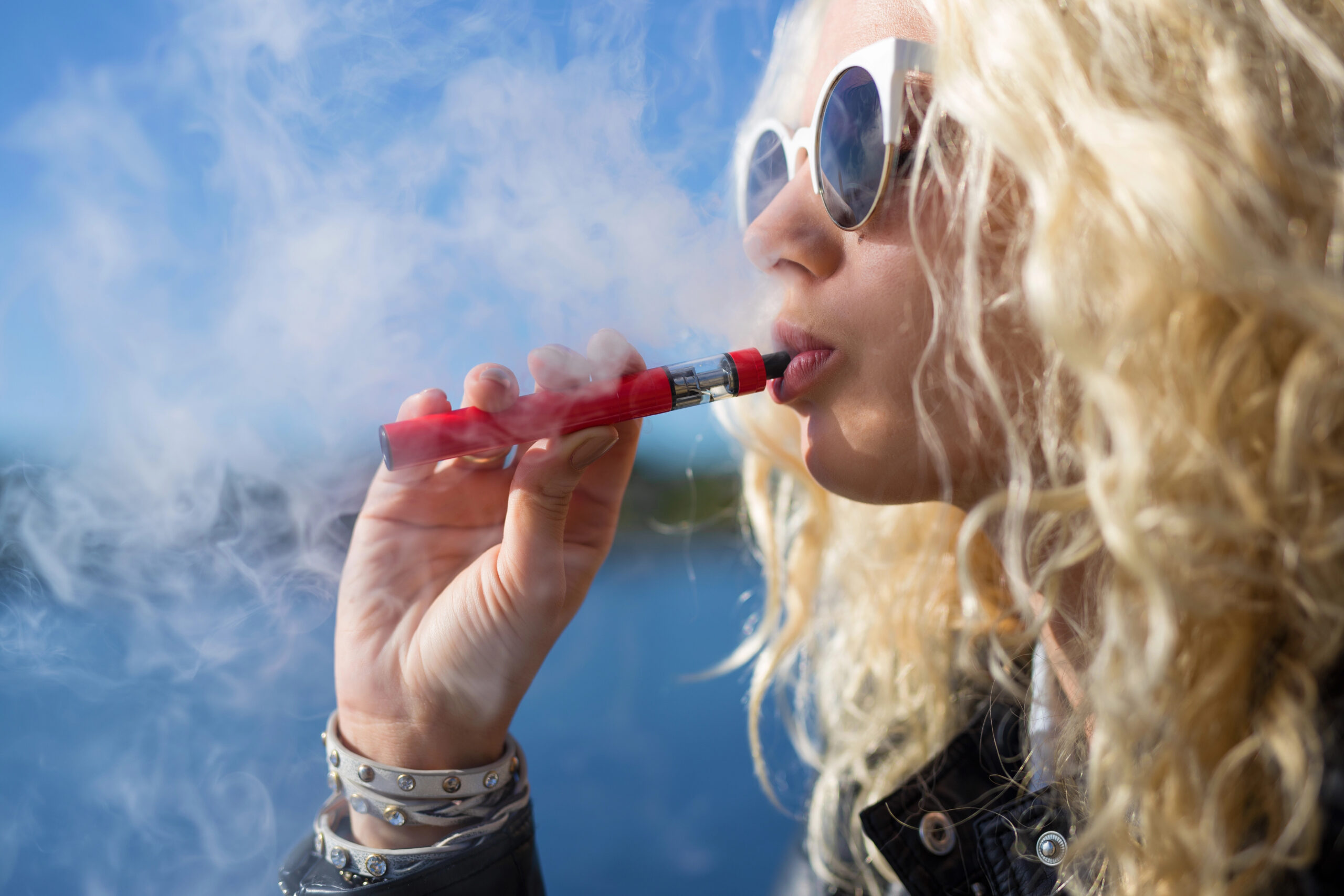 Person vaping outdoors with a blue sky background.