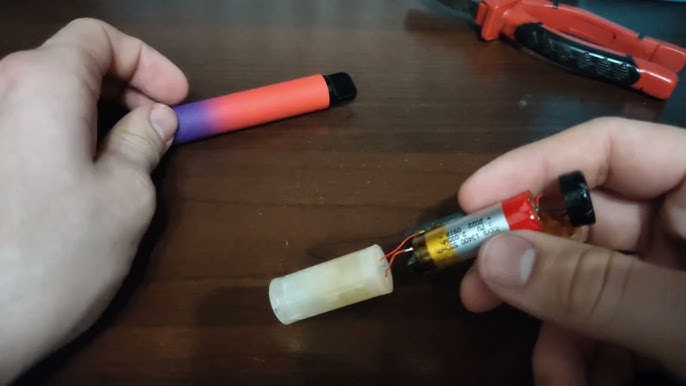 E-papieros leżący na drewnianym biurku, podłączony kablem USB do standardowej białej kostki wpiętej do gniazdka, z otoczeniem wolnym od materiałów łatwopalnych.
