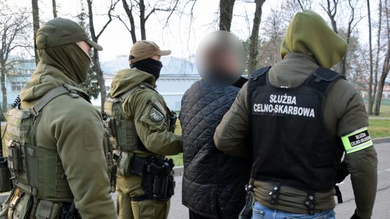 Zatrzymana paczka z e-papierosem (box mod) na stole celnika, obok brakująca banderola, dokumenty kontroli celno-skarbowej, sugerująca konsekwencje braku akcyzy.