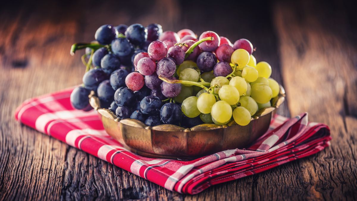 Bowl of assorted grapes on a red checkered napkin.