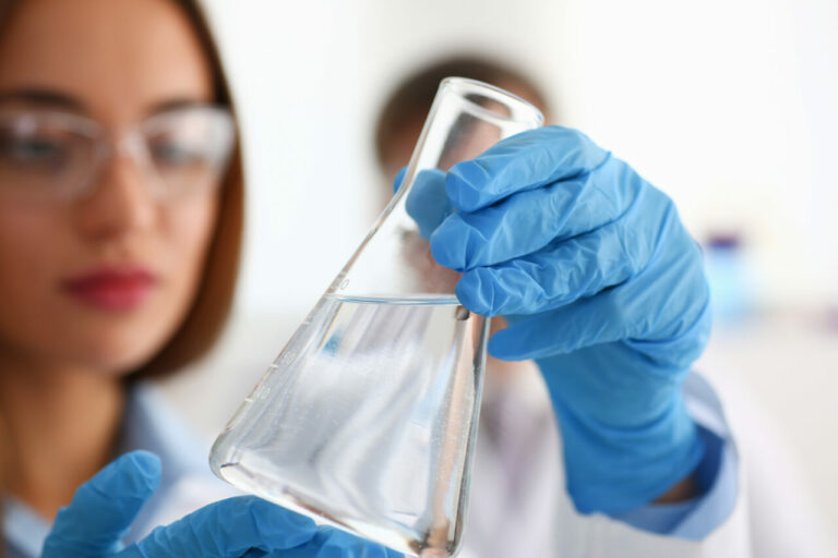 Naukowiec w kitlu laboratoryjnym, trzymający fiolkę z kolorowym e-liquidem w laboratorium, z widocznym sprzętem do analizy smaków, podkreślającym ciekawość i eksperymenty.