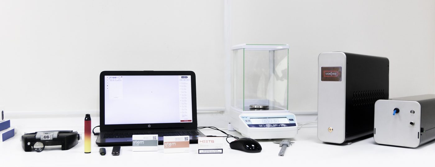 Ujęcie wnętrza nowoczesnego laboratorium z precyzyjnym sprzętem do testowania e-papierosów i produktu Fizzy Twins na stole laboratoryjnym.