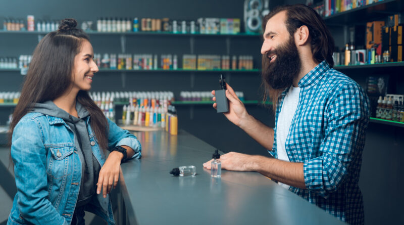 Bliskie ujęcie na obszerną ścianę w sklepie vape, wypełnioną setkami kolorowych buteleczek z liquidami e-papierosowymi, symbolizującą duży wybór.