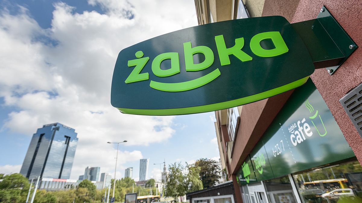 Panorama polskiego miasta z widocznymi w różnych miejscach charakterystycznymi zielonymi szyldami sklepów Żabka, podkreślająca ich wszechobecność.