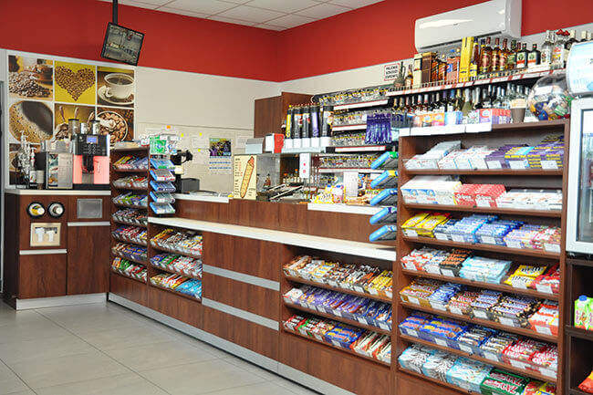 Scena w sklepie Żabka, gdzie klient pyta kasjera o konkretny produkt (e-papierosy 20000 buchów), a kasjer patrzy na niego zdezorientowany, obok półki z małymi, prostymi jednorazówkami.