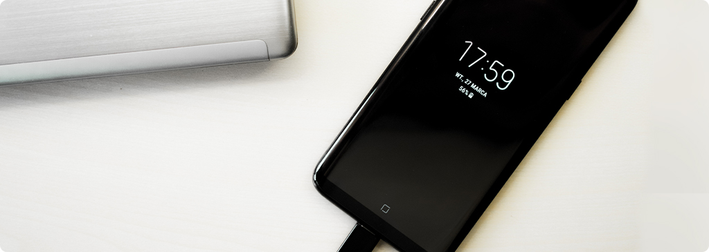 Ilustracja przedstawiająca osobę zaniepokojoną, patrzącą na ikonę rozładowanej baterii na urządzeniu, symbolizująca