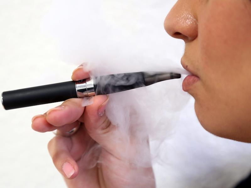 Osoba vapująca na przystanku autobusowym, z wyraźnym znakiem zakazu vapowania w tle i zbliżającym się strażnikiem miejskim, podkreślającym ryzyko mandatu.