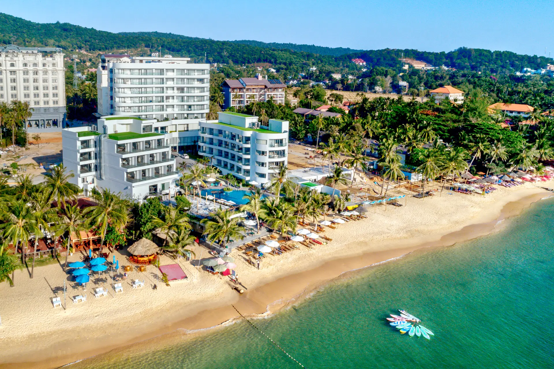 Osoba wychodząca ze sklepu Żabka z torbą, trzymająca w ręku hot-doga, puszkę energetyka i małego, kolorowego e-papierosa jednorazowego.