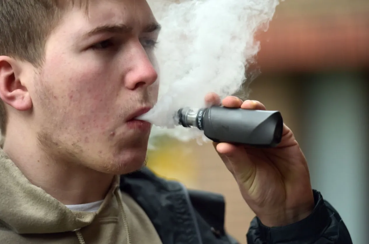 vapowanie przed kinem, palenie e-papierosa na zewnątrz, przerwa na vape przed filmem, osoba używająca e-papierosa outdoor, przygotowanie do seansu vape - Wapowanie może uszkadzać płuca. E-papierosy podnoszą poziom stresu ...